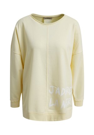 Light yellow long-sleeve sweatshirt with round neckline, central seam, and partial white text "JADIRE LA NIR" on the lower front right side.