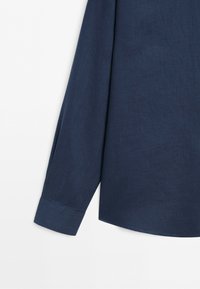 Long sleeve cuff of a dark blue linen shirt on a white background.