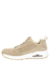 Beige suède sneakers met geperforeerde details, een witte tussenzool, een bruine rubberen zool en transparante luchtkussens aan de zijkant.