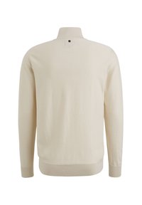 Beżowy sweter z długim rękawem i wysokim kołnierzem, wykonany z prążkowanej tkaniny. Posiada małą metkę z tyłu na szyi oraz prążkowane mankiety i dół.