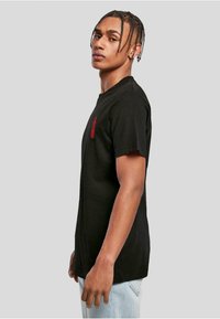 Black cotton t-shirt with short sleeves, featuring a red graphic on the left chest. Straight cut and comfortable fit, paired with light blue jeans.