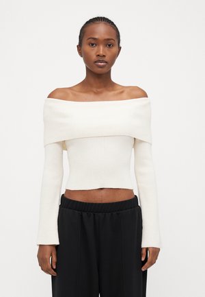 Off-the-shoulder, ribbed knit crop top in off-white; features long sleeves with a fitted bodice and raw hem, paired with black pants.