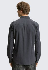 Langärmliges, dunkelgraues Hemd mit strukturiertem Finish, Knopfmanschetten und Kragen. Auf der Rückseite befindet sich ein Einsatz und saubere Nähte.