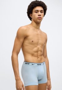 Φωτεινά γαλάζια ανδρικά εσώρουχα Nike σε στυλ boxer με μαύρη μέση που φέρει το λογότυπο της Nike. Το ύφασμα φαίνεται λείο με εφαρμοστή σχεδίαση.
