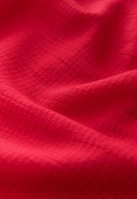 Roter, strukturierter Stoff mit einem Schachbrettmuster, der glatte, weiche Wellen und eine satte, lebendige Farbe zeigt.