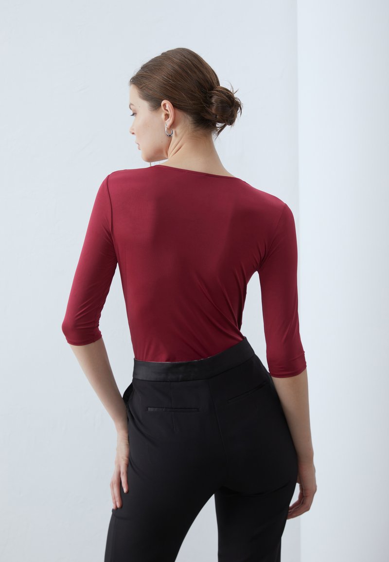Top bordeaux a maniche lunghe con scollatura tonda, abbinato a pantaloni neri sartoriali con una vita liscia e tasche posteriori.
