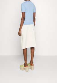 Light blue short-sleeve knit top, white A-line skirt, and green platform clogs with a woven base, viewed from the back.