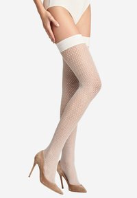 Calze a rete bianche fino alla coscia con un'ampia fascia bianca nella parte superiore. La modella indossa scarpe con tacco alto color beige. La texture è aperta e simile a una rete.