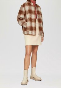 Plaid jacket in brown and cream, beige skirt, and beige ankle boots. Textured fabric, loose fit, and high neckline on the jacket.