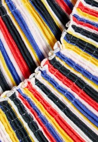 Kangas berwarna-warni yang menampilkan garis-garis tipis dengan tekstur dalam warna merah, biru, kuning, hitam, dan putih dengan detail tepi berkerut.