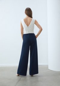 Vit ärmlös topp med djup V-back, kombinerad med högmidjade marinblå vida byxor som har en slät textur och en elegant design.