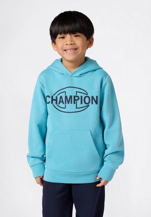 Un sweat à capuche bleu clair en tissu doux, arborant un grand logo « CHAMPION » navy à l'avant et une poche frontale.