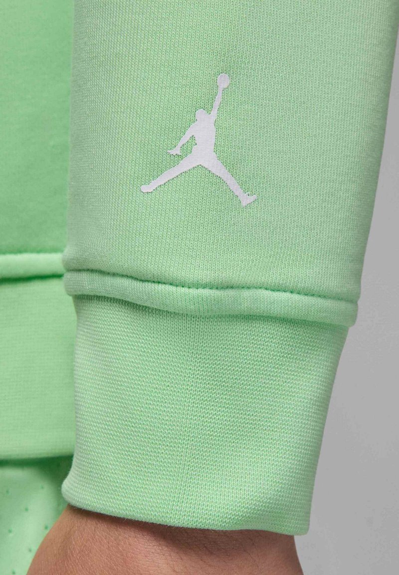 Hellgrüner Sweatshirtstoff mit gerippten Bündchen, versehen mit einem weißen Jumpman-Logo. Glatte Textur, lockerer Schnitt und einfaches Design.