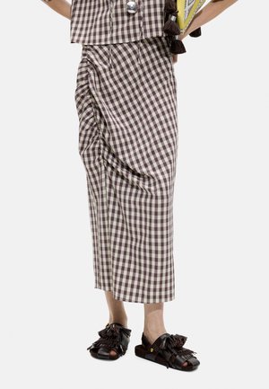 Dolna część ciała ubrana w brązowo-białą kratowaną marszczoną spódnicę w połączeniu z czarnymi sandałami z odkrytymi palcami, zdobionymi frędzlami i chwostami.