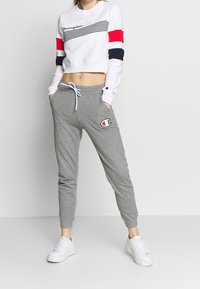 Vit kortärmad sweatshirt med ärmar i marinblått och rött randigt mönster, matchat med grå sweatpants med logopatch och snörningsmidja. Vita sneakers.