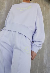 Fialový sweatshirt a kalhoty ze směsového bavlněného materiálu s nápisem "Buď laskavý" a logem Nike v reflexní neonově žluté barvě. Volný střih, žebrované manžety, měkká textura.