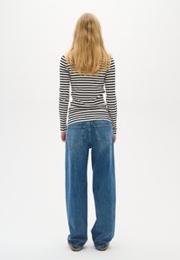 Maglia a maniche lunghe a righe bianche e nere abbinata a jeans di jeans blu a gamba larga, vista da dietro.