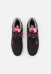 Sneaker nere e rosse con tomaia in suede, colletto imbottito e suola bianca. Presentano il logo sulla linguetta e sul lato, con lacci neri e dettagli.