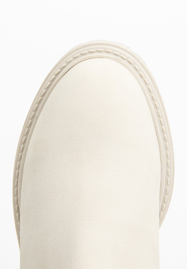 Bottine en suede blanche avec une finition lisse, un embout rond et des coutures visibles le long de la semelle. Design minimaliste, sans embellissements.