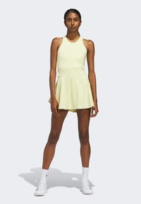 Vaaleankeltainen urheiluasu, jossa on istuva yläosa ja liehuva hame. Yhdistetty valkoisten tennareiden ja sukkien kanssa, näyttäen sileältä ja joustavalta kankaalta.