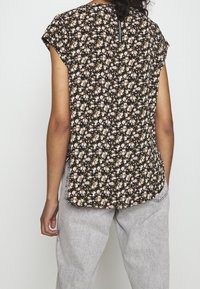 Top nero a maniche corte con un motivo floreale in rosa e bianco, dotato di una cerniera sul retro e di un orlo curvato, abbinato a pantaloni grigi.