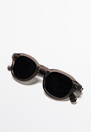 Dunkel getönte, übergroße Sonnenbrille mit transparentem grauem Gestell. Verfügt über abgerundete Gläser, flache Bügel und ein einzigartiges geometrisches Design.