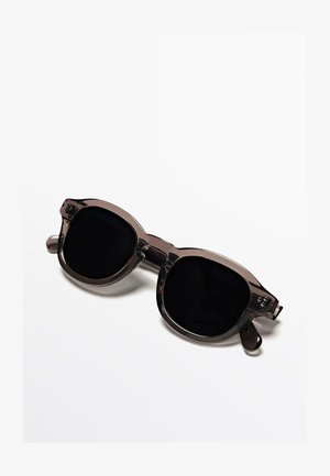 Occhiali da sole oversize con lenti scure e montatura trasparente grigia. Caratterizzati da lenti arrotondate, aste piatte e un design geometrico unico.