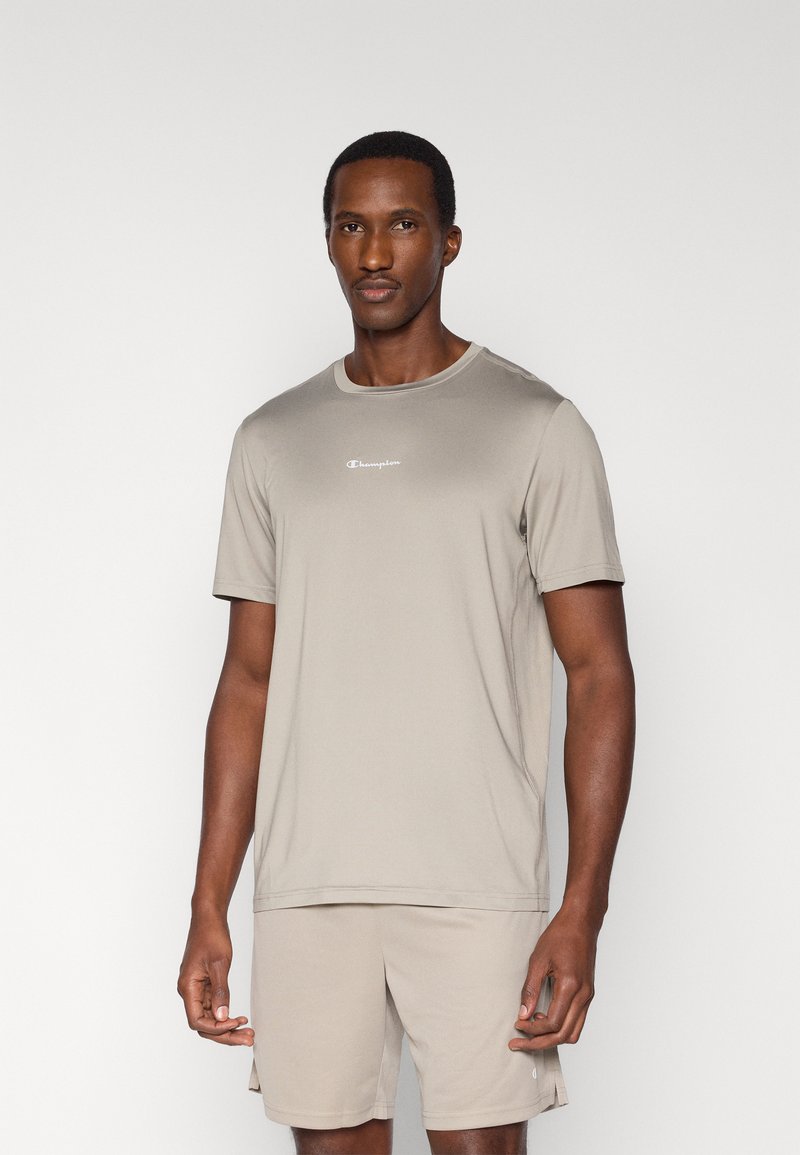 Αθλητική μπλούζα σε ανοιχτό μπεζ χρώμα από απαλό ύφασμα, με κοντά μανίκια και στρογγυλή λαιμόκοψη, με μικρό λευκό λογότυπο στο στήθος.