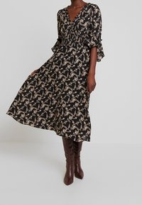 Black floral dress with a V-neck, gathered waist, and flared sleeves. Paired with knee-high burgundy boots for a contrast in colors.