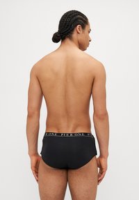 Schwarze Schwimmbrieftaschen mit elastischem, gebrandetem Bund. Hergestellt aus einem glatten Material, mit eng anliegendem Design und minimaler seitlicher Abdeckung.