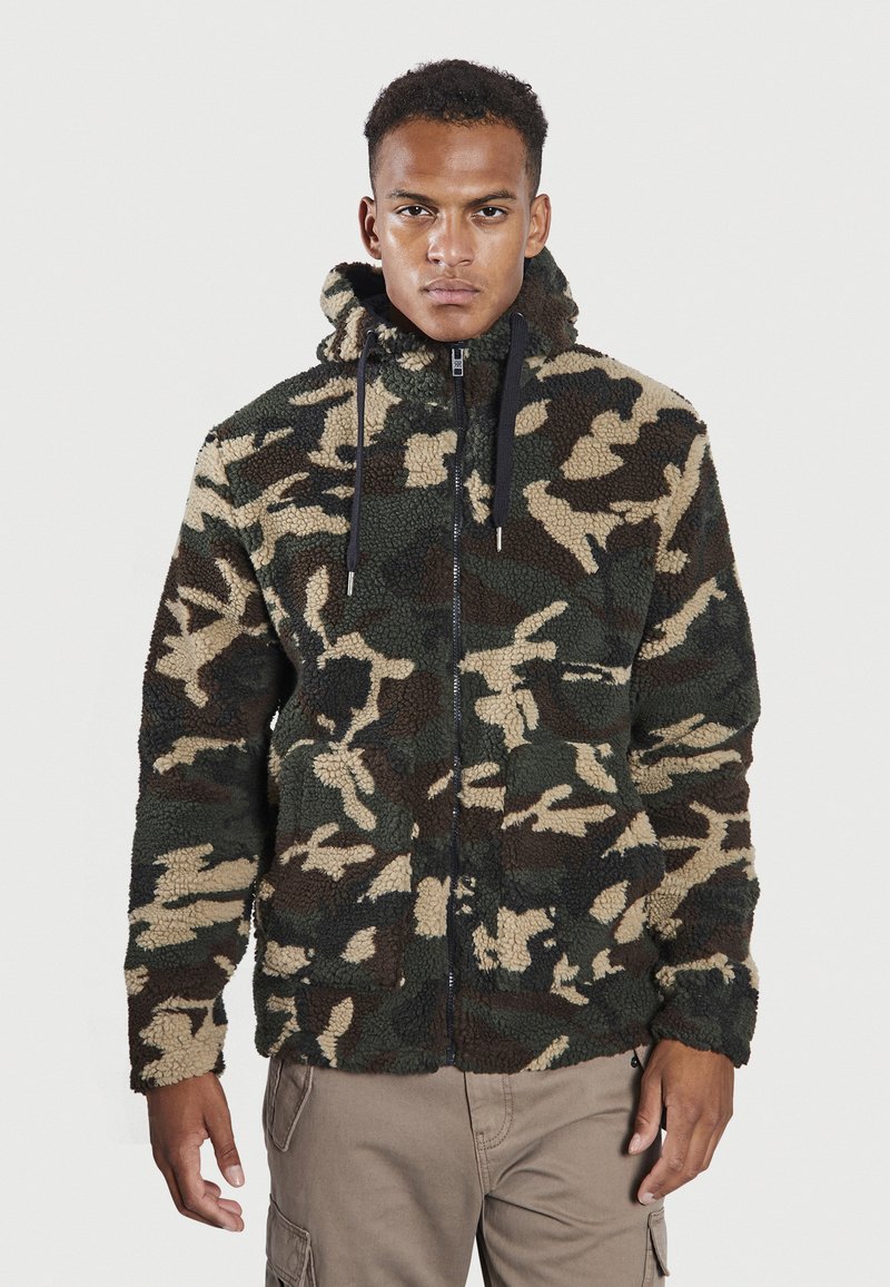 Sudadera de forro polar en patrón de camuflaje con colores verde, marrón y beige. Cuenta con cierre de cremallera, capucha ajustable y tejido texturizado.