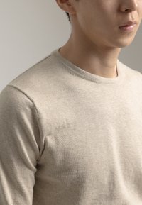 Camisa de punto de manga larga beige con escote redondo. Textura suave y diseño ajustado, que muestra la parte superior del pecho y los hombros.