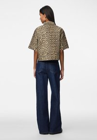 Jaqueta cropped com padrão de onça, com gola, mangas curtas e barra preta sólida, combinada com jeans escuros de perna larga.