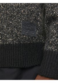 Pull in maglia grigio scuro caratterizzato da un motivo testurizzato, polsini elasticizzati a coste e un'etichetta nera con un'emblema a forma di globo.