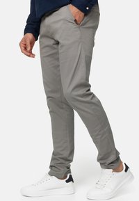 Jasnoszare chinos w slim fit z bocznymi kieszeniami, w połączeniu z białymi sneakersami z granatowymi akcentami. Gładka tekstura i swobodny design.