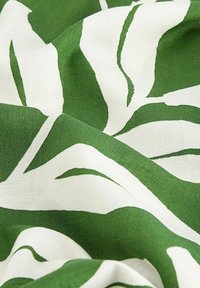 Tissu blanc avec de grands motifs de feuilles abstraites vertes, légèrement froissé et à la texture douce.