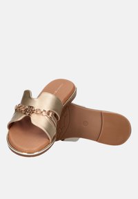 Las sandalias de dedo metálicas doradas cuentan con una amplia correa con un detalle de cadena entrelazada. La suela es marrón y tiene un patrón de agarre texturizado.