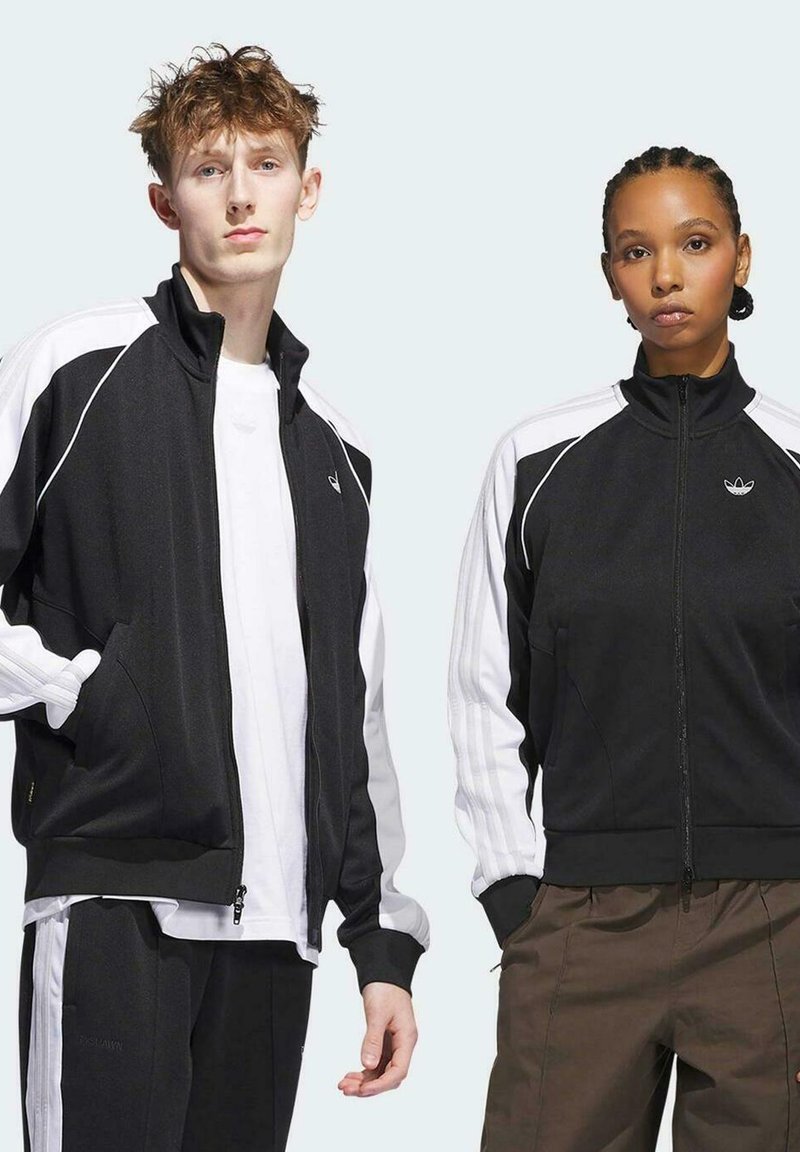 Chaquetas de pista en blanco y negro con cremallera, cuellos altos y acentos a rayas. Pantalones negros, camisetas blancas debajo. Tejido texturizado.