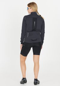 Svart cykeljacka med hög krage, långa ärmar och reflekterande detaljer. Bärs tillsammans med svarta cykelshorts och skor med en strömlinjeformad design.