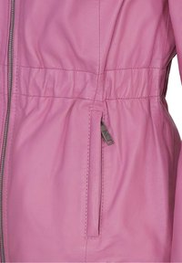 Gros plan d'une veste en cuir rose montrant une poche verticale zippée et des fronces à la taille.