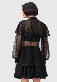 Μαύρο φόρεμα από δαντέλα με στρωμένα, βολάν μανίκια, διαφανές σώμα με τονισμένη μέση και φούστα με βολάν σε στρώσεις.