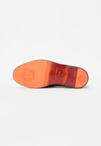 Podošva topánky s hladkým čiernym okrajom, stredná časť z oranžovej kože, vygravírované logo a textúrované vzory. Obsahuje označenú veľkosť a branding.