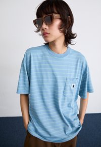 Lyseblå stribet T-shirt med rund halsudskæring, korte ærmer og en brystlomme med et logo. Stoffet ser blødt og afslappet ud.