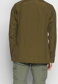 Olivgrön lättviktsjacka med lång ärm och rak skärning, tillverkad av slät, vattenavvisande material. Inga synliga dekorationer.