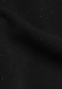 Gros plan sur un tissu noir à texture finement côtelée avec de petites taches blanches dispersées à la surface.