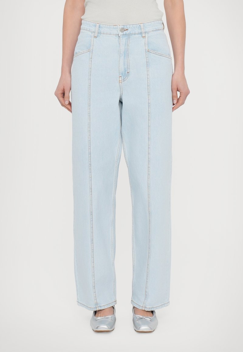 Jean large en denim bleu clair avec une taille haute, épaisses coutures latérales et un design à cinq poches. Texture douce avec des coutures contrastées légères.