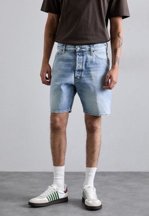 Lichtblauwe denim shorts met een vervaagd ontwerp, vijf zakken en een knoopsluiting. Draag ze met witte sokken en witte sneakers met groene accenten.