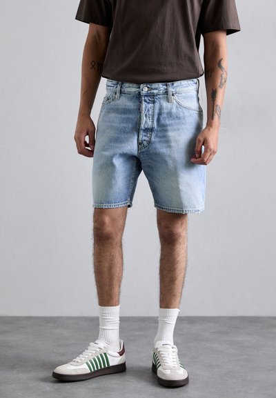 Shorts in denim azzurro chiaro con un design sbiadito, cinque tasche e chiusura con bottone. Indossati con calzini bianchi e sneakers bianche con dettagli verdi.