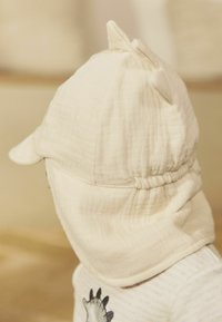 Off-white Baumwollmütze mit zwei spitzen Ohren, einem gebogenen Schirm und einem gerafften Nacken für einen engen Sitz, kombiniert mit einem gestreiften Textilhemd.