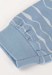 Manche en tissu bleu clair avec des rayures ondulées blanches, dotée d'un poignet côtelé et de fronces près du poignet.